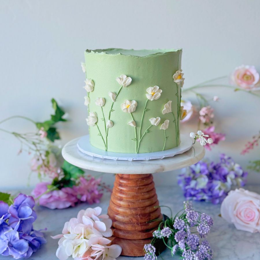 Green cake with floral decorations on a marble stand with flowers in the background