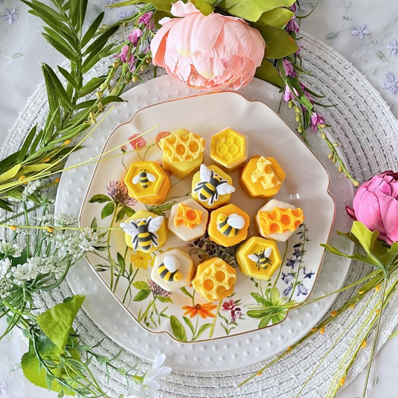 Plate of yellow floral-themed pastries garnished with tiny white flowers and leaves, styled with greenery and peonies