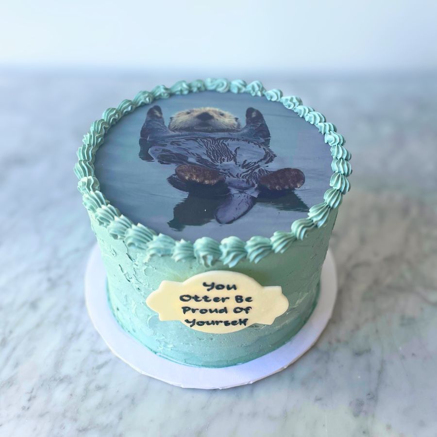 Cake with an image of an otter at the top and 'You Otter Be Proud Of Yourself' message on a marble surface