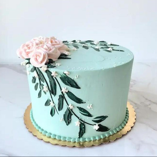 A light blue cake decorated with a pink flower and green leaves on the side.