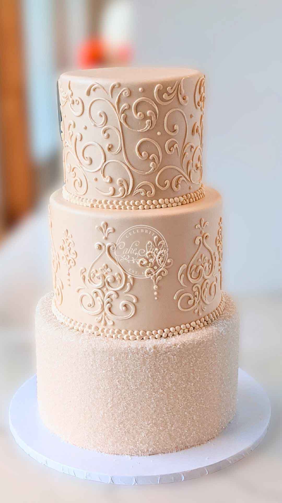 A three-tiered cake with an intricate gold design on the top and a smooth, light peach bottom.
