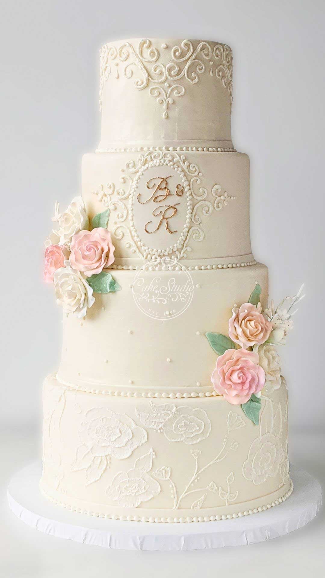 A four-tiered white wedding cake decorated with small pink and white flowers and gold accents.