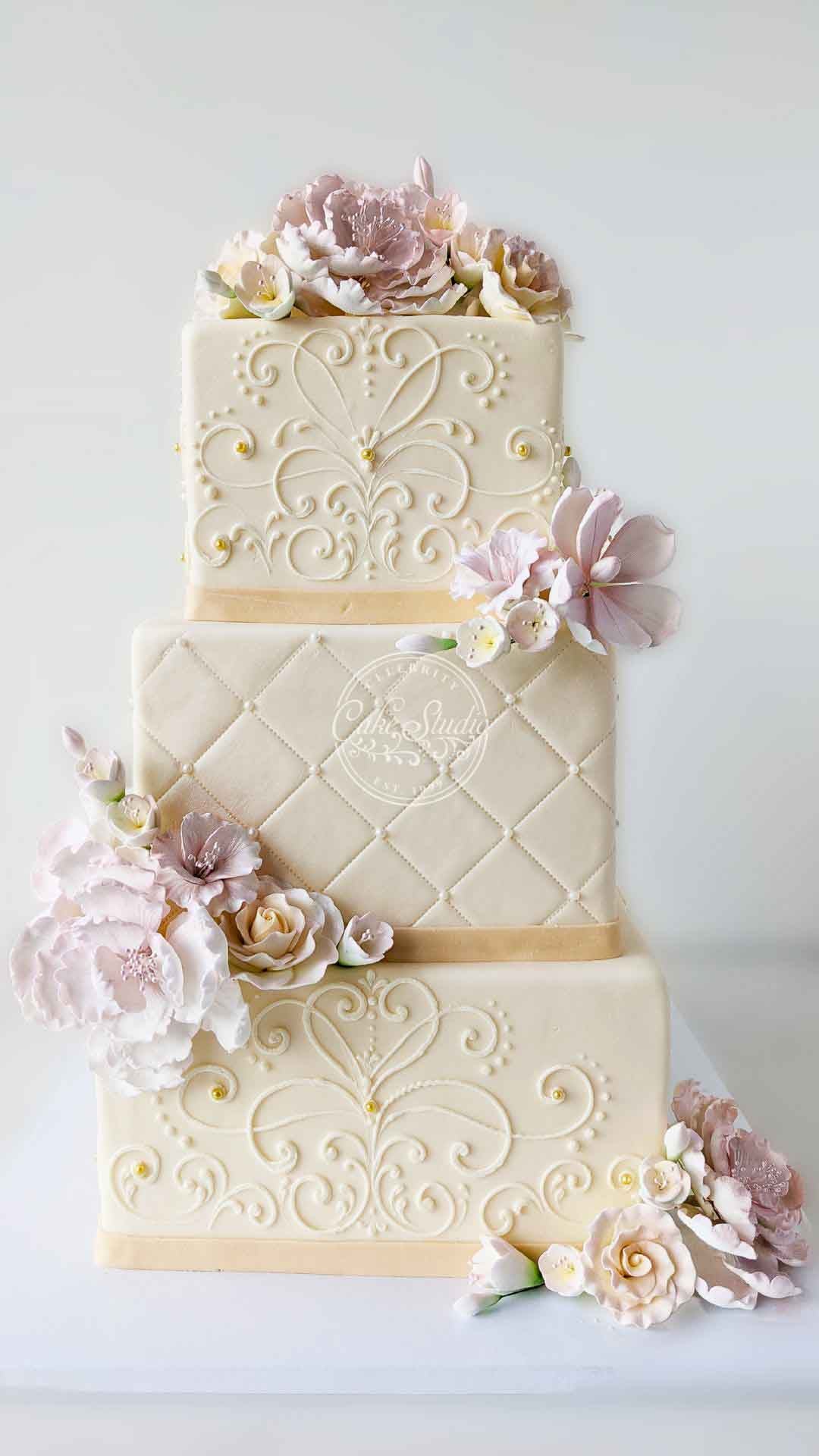 A three-tiered white wedding cake with pink flowers cascading down on every corner.