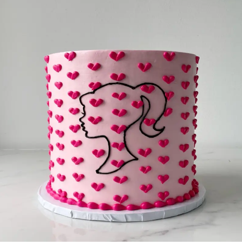 A pink cake with small dark pink hearts and a black outline of a Barbie head