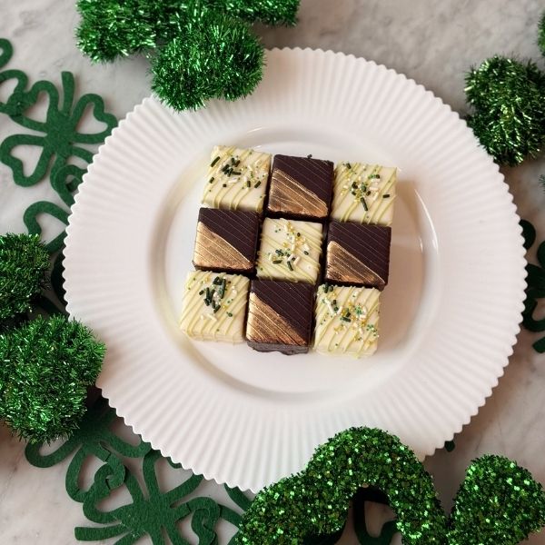Square pieces of chocolate and vanilla petit fours on a white plate with green decorative elements.
