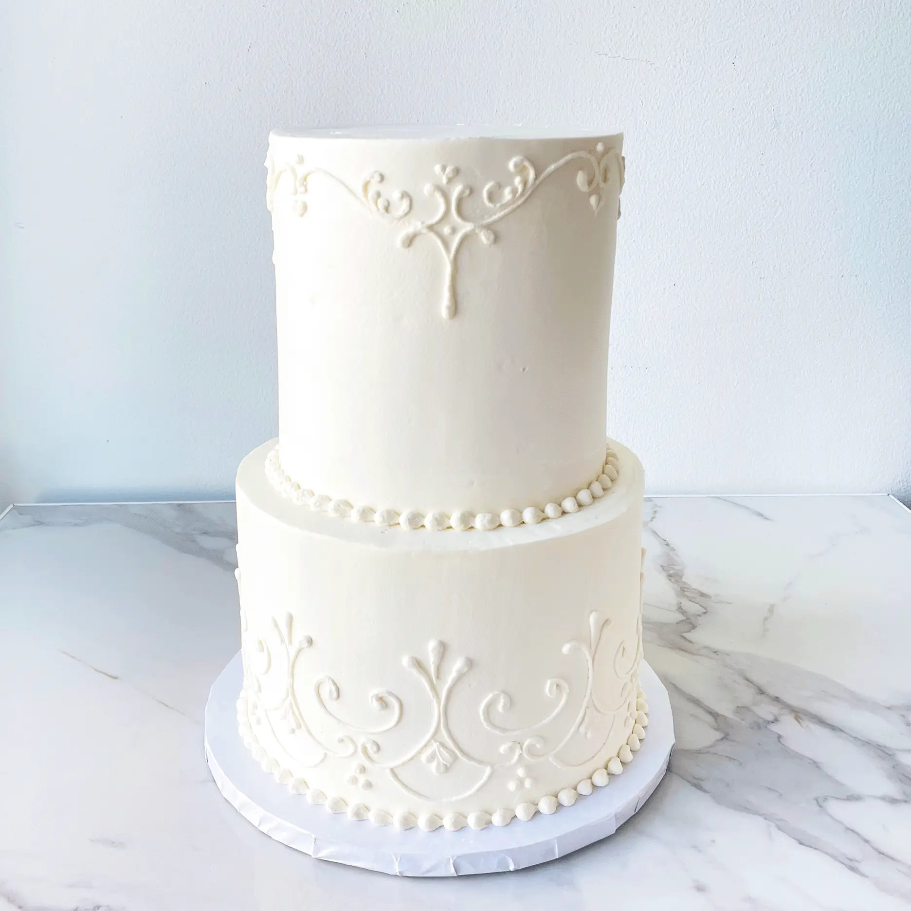 A two-tiered white cake with a detailed, textured design on both layers.