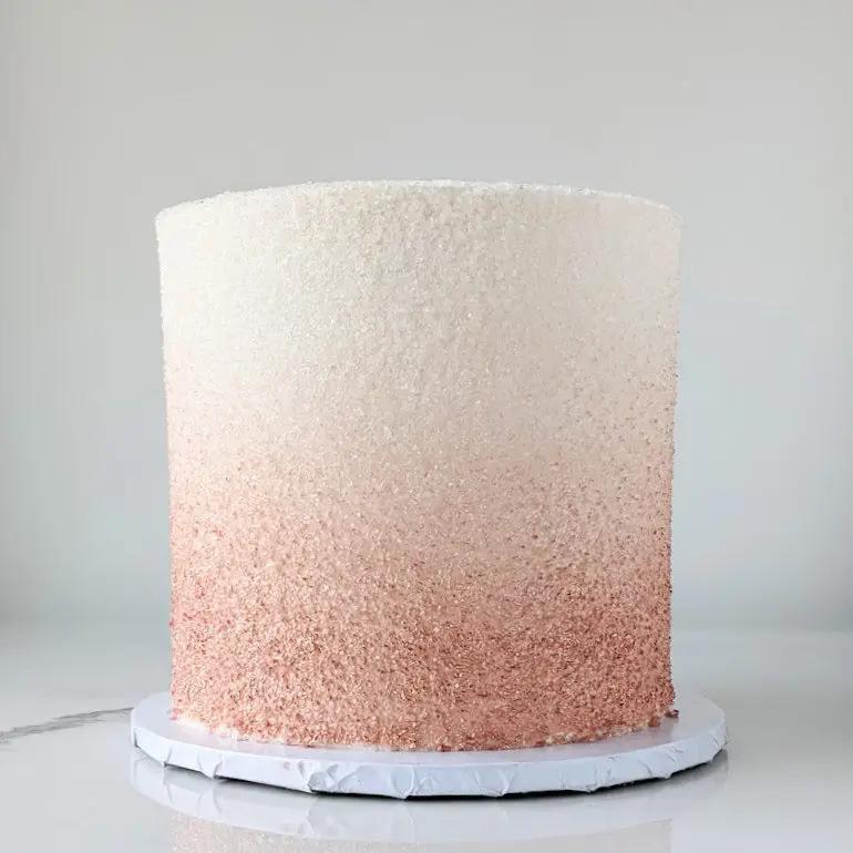A round, single-tiered cake with an ombre frosting that transitions from a dark pink at the bottom to a light pink at the top.