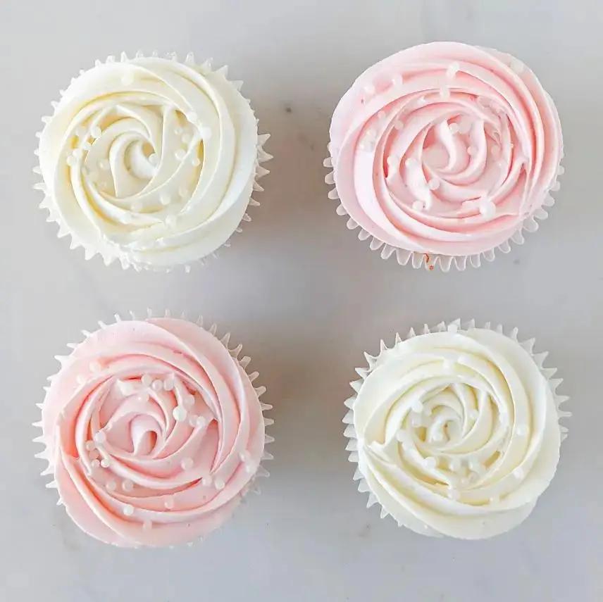 A top-down view of four cupcakes arranged in a square. Two have pink frosting and two have white or very light-colored frosting, each swirled into a rose.