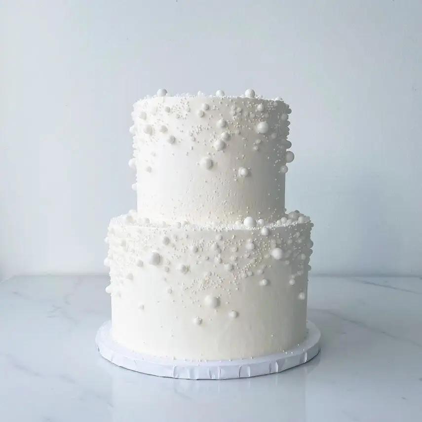 A two-tiered cake with white frosting. The cake is decorated with small white edible pearls scattered across both tiers.
