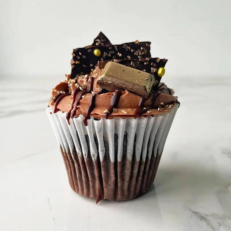 A chocolate cupcake with chocolate frosting and chocolate bar, and gold flecks.