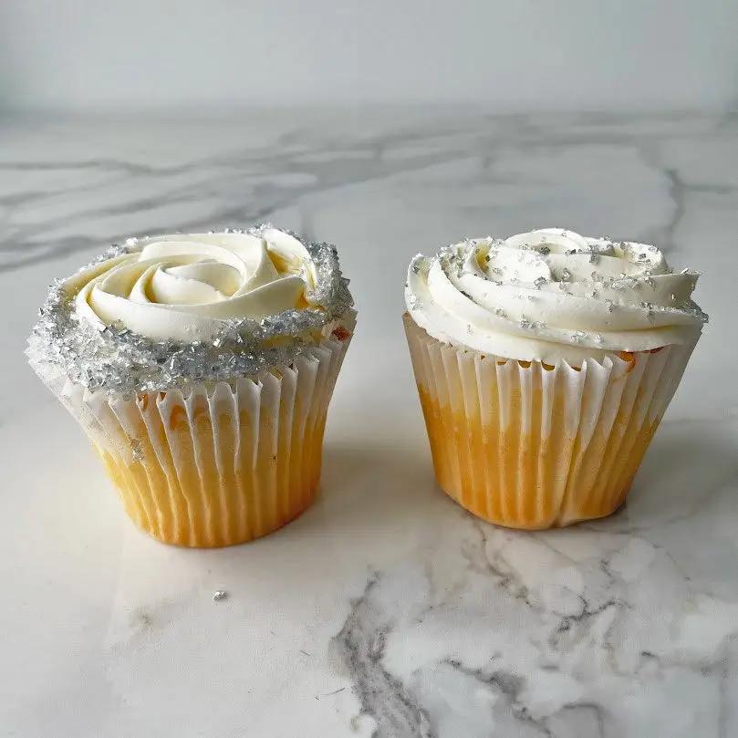 Two cupcakes with white frosting and silver flecks decorations.