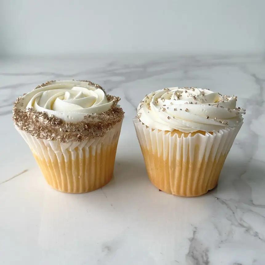 Two cupcakes with white frosting, one with gold sprinkles and one with silver few sprinkles.
