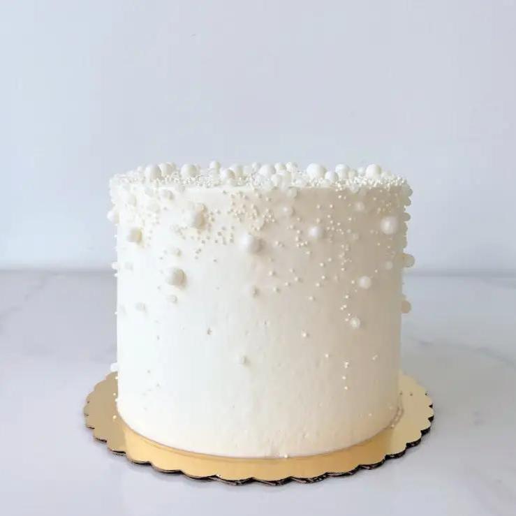 A small, single-tiered cake with white frosting decorated with small white sprinkles or edible pearls.