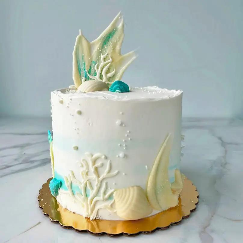 An Ocean-themed white cake with the design of seashells, corals, and pearls.