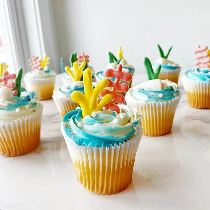 Dozen cupcakes with blue frosting and tropical-themed decorations.