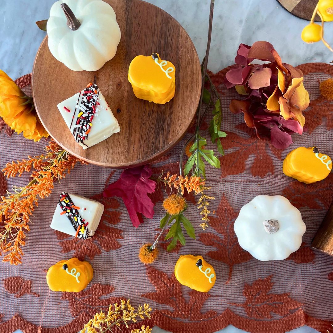 Autum-themed square cake with a chocolate drizzle and sprinkles, and a few small pumpkin-shaped cakes.
