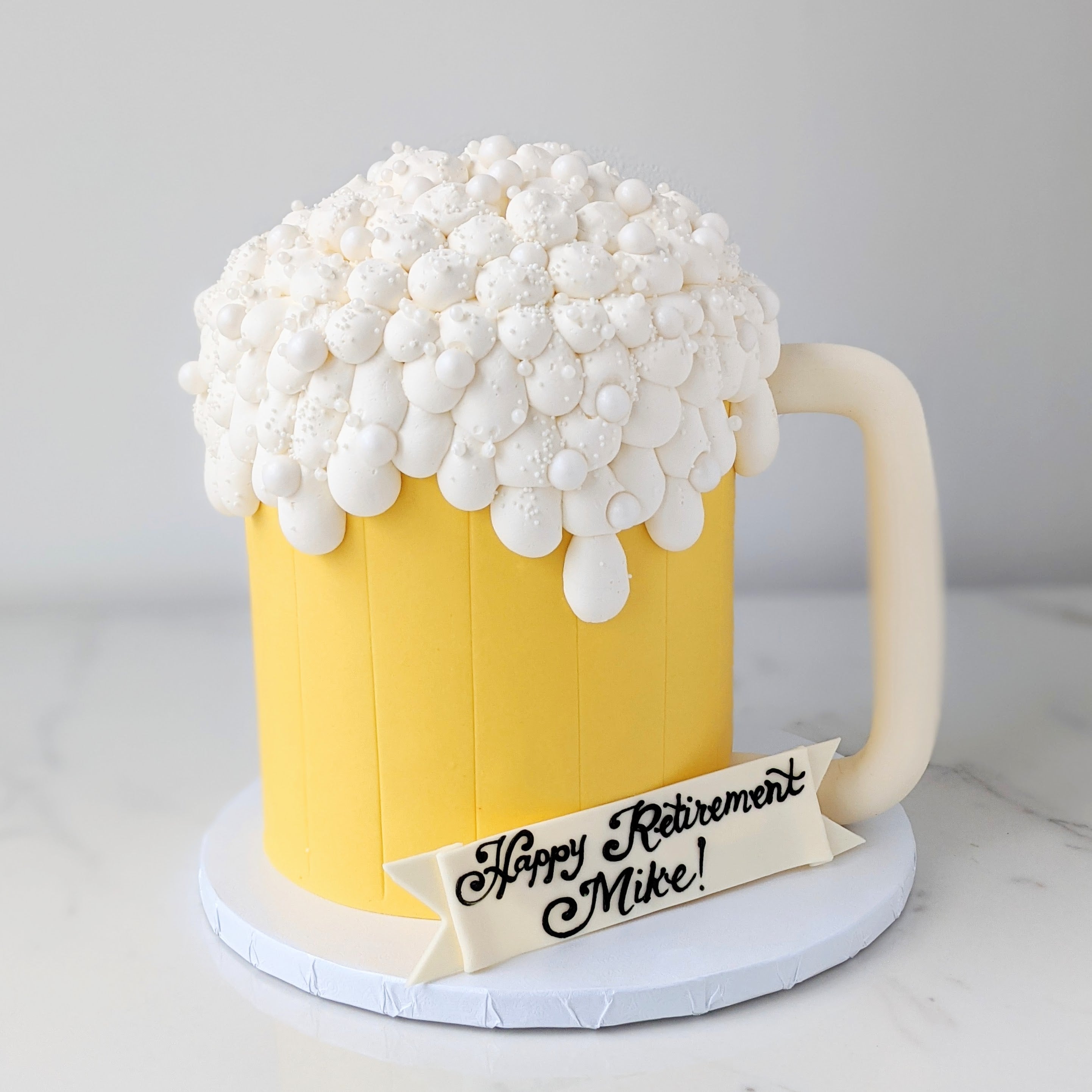 Beer mug cake with white foam and 'Happy Retirement Mike!' sign 