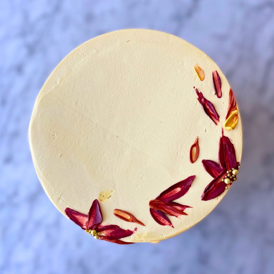 An overhead view of a round cake with pale yellow frosting, decorated with small painted autumn leaves in shades of red, orange, and yellow.
