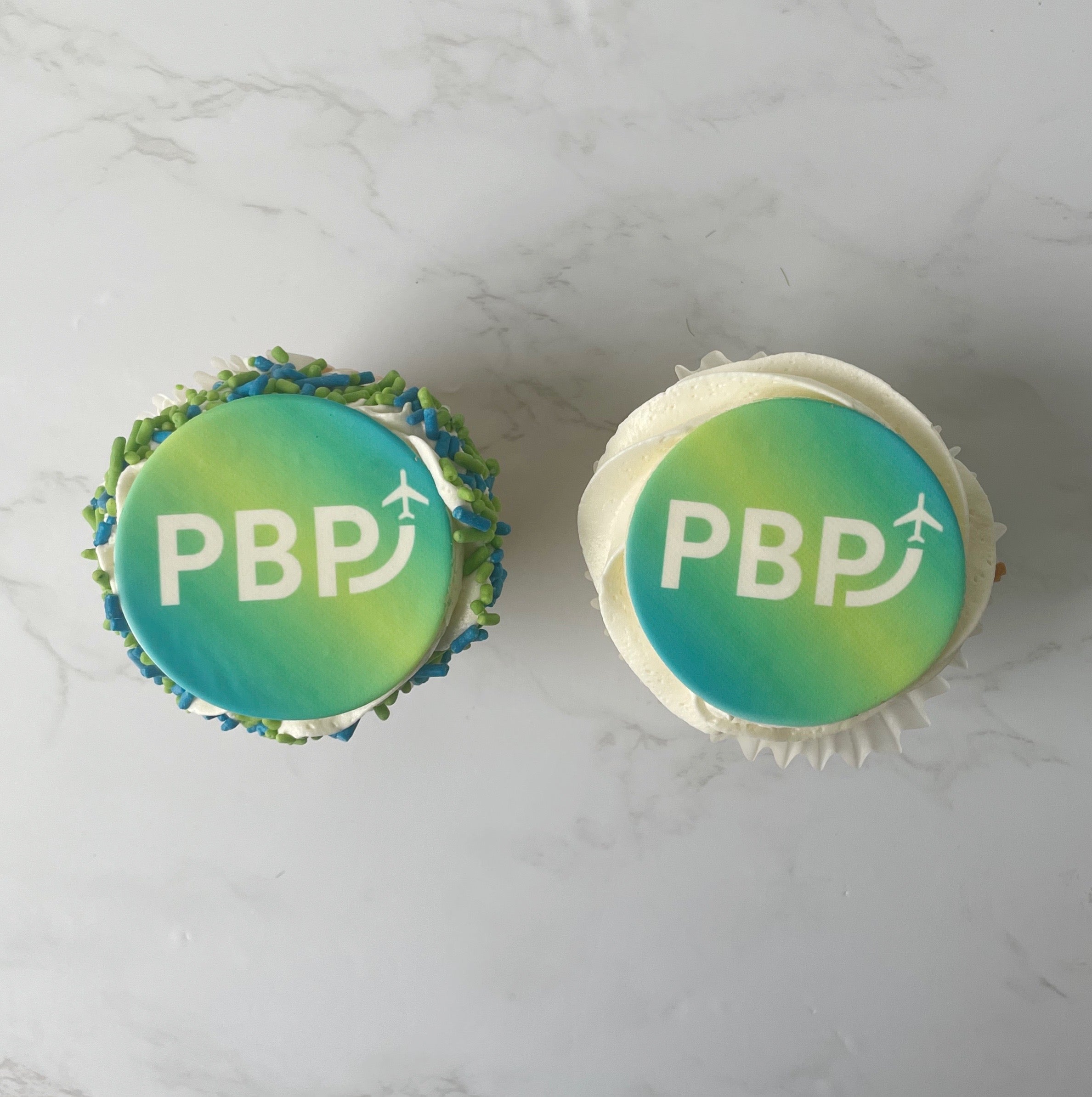Two cupcakes with 'PBP' branding on a marble surface