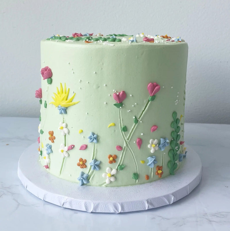 Green buttercream cake decorated with spring flowers and piping details