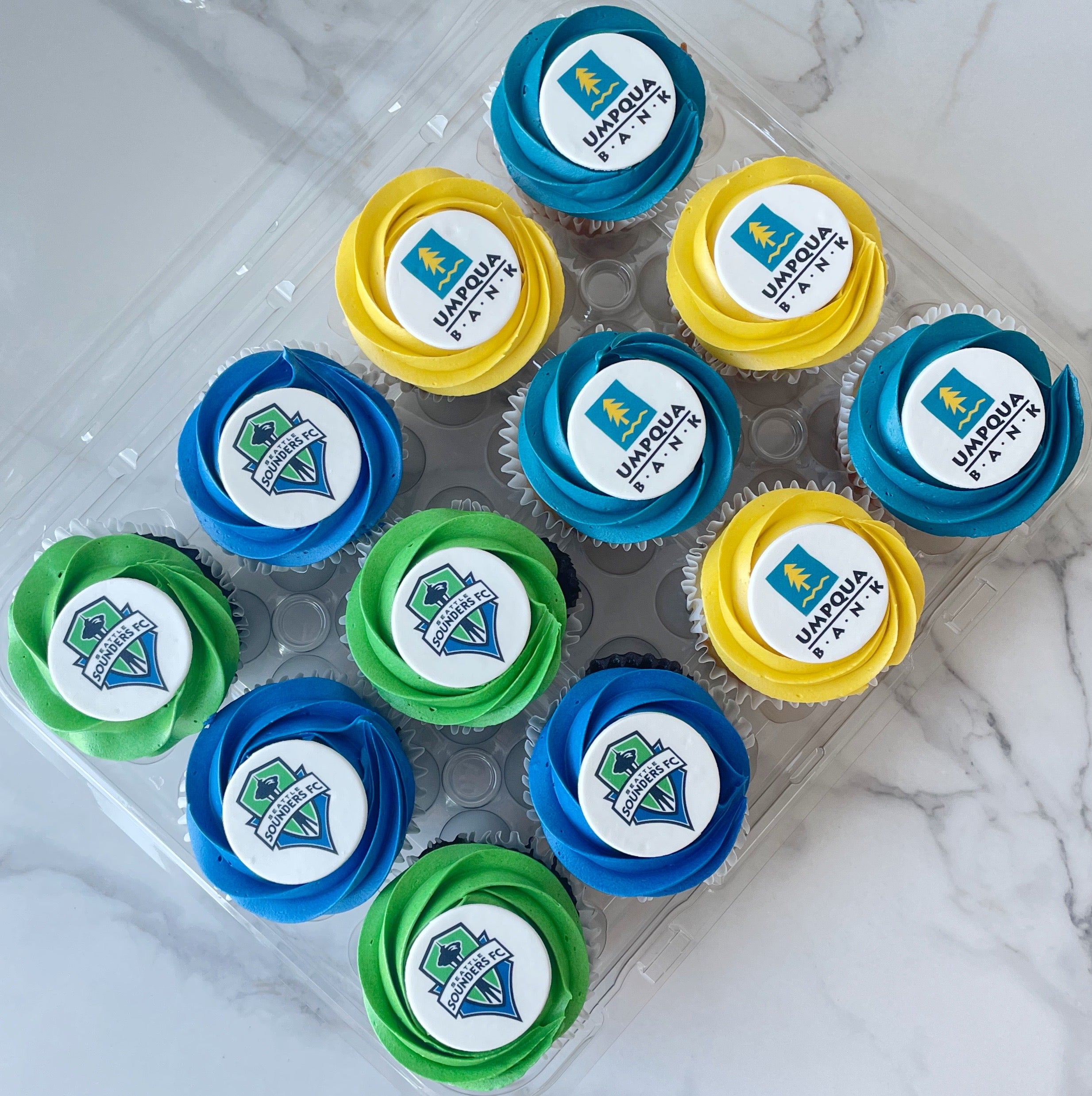 Cupcakes with Umpqua Bank logo in a clear container on a marble surface