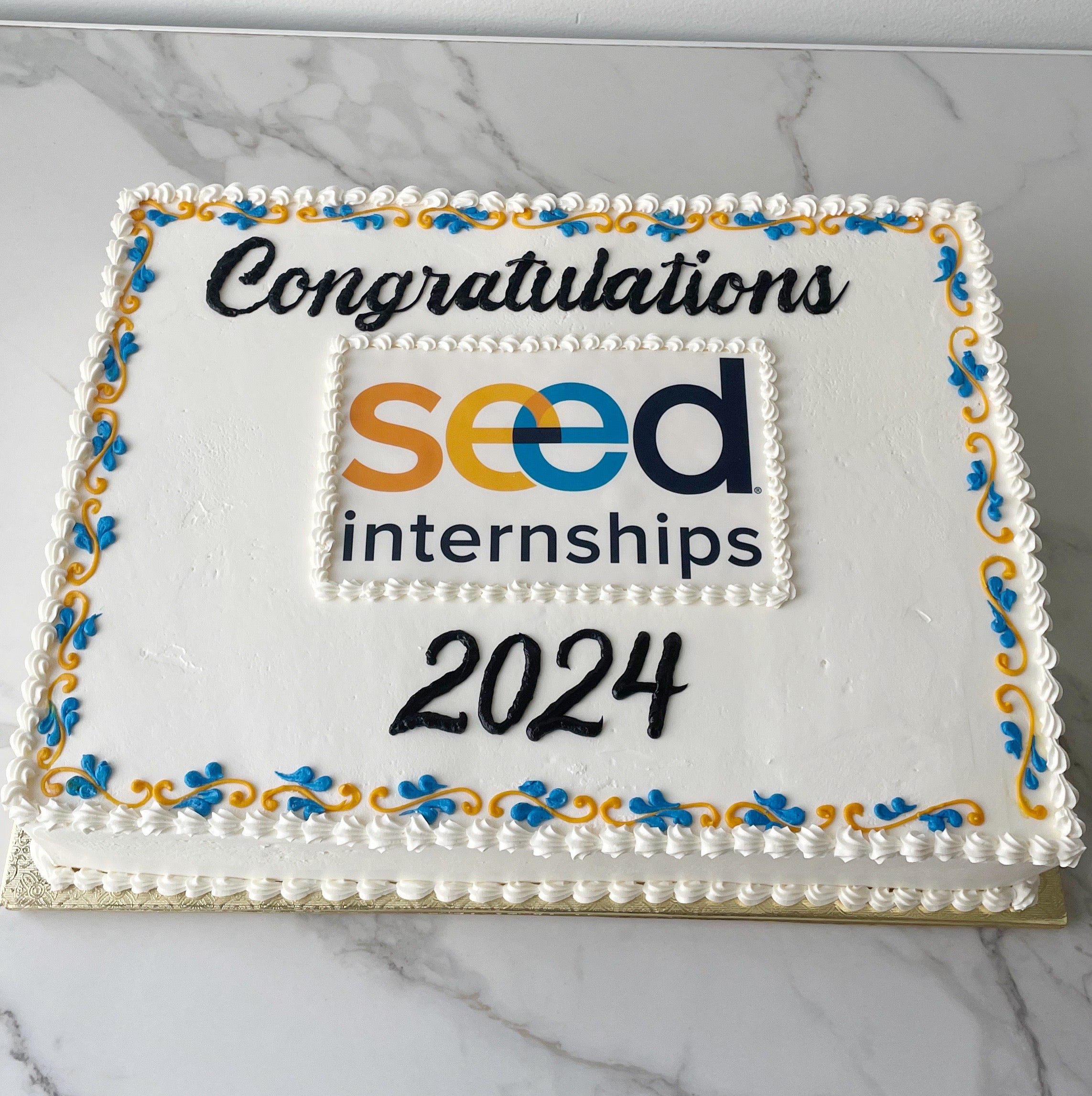 Sheet cake with 'Congratulations seed internships 2024' text and logo on a marble surface