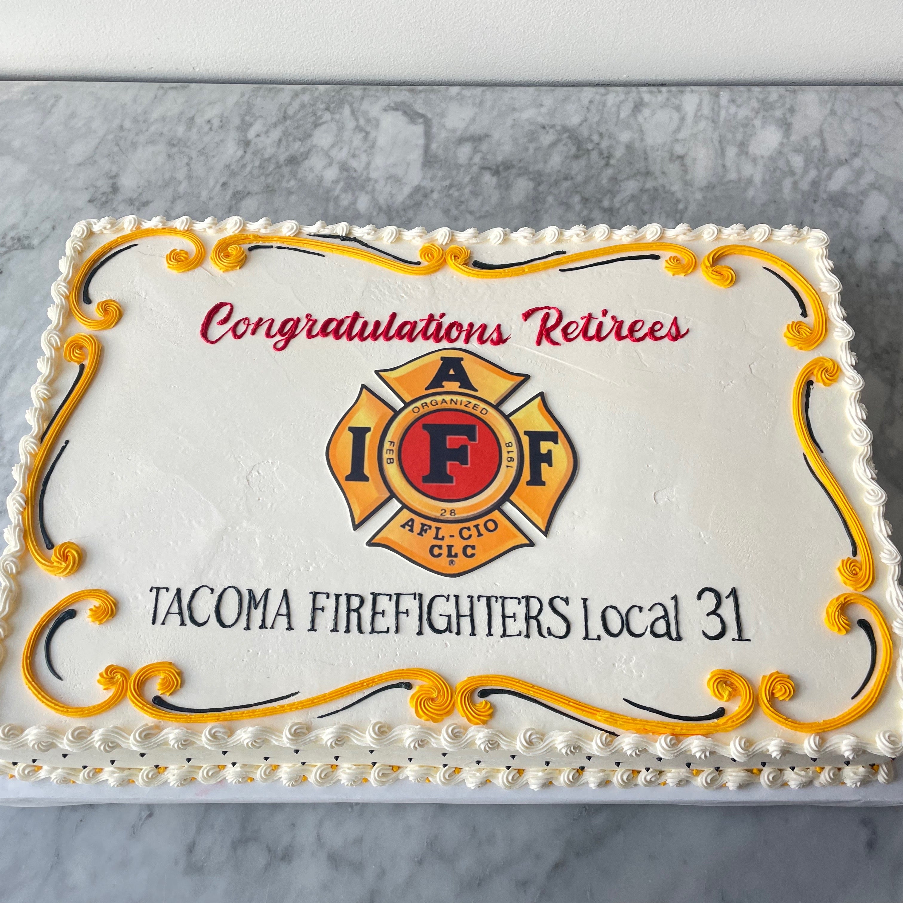 Sheet cake with 'Congratulations Retirees' text and Tacoma Firefighters Local 31 logo on a marble surface.