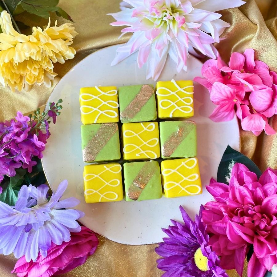 yellow and green square petit fours surrounded by colorful flowers on a gold fabric background