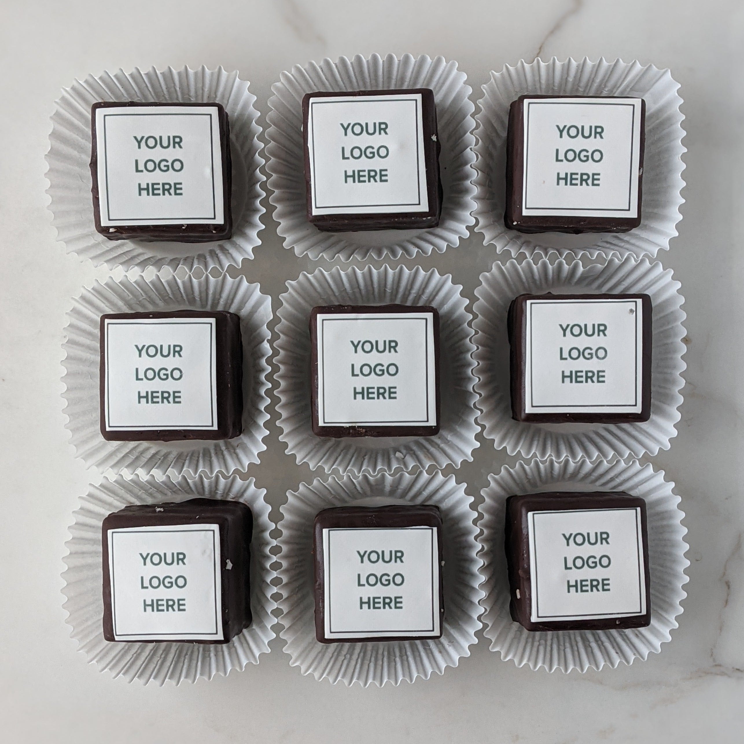 Chocolate cupcakes with custom logo labels on a marble surface