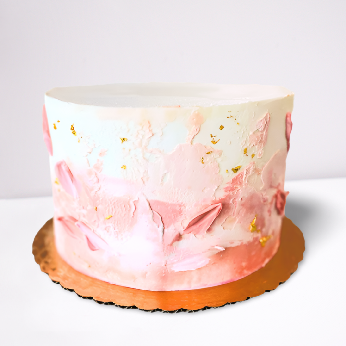 A round cake with white frosting that has a watercolor effect of various shades of pink. The cake has gold flecks on its sides.
