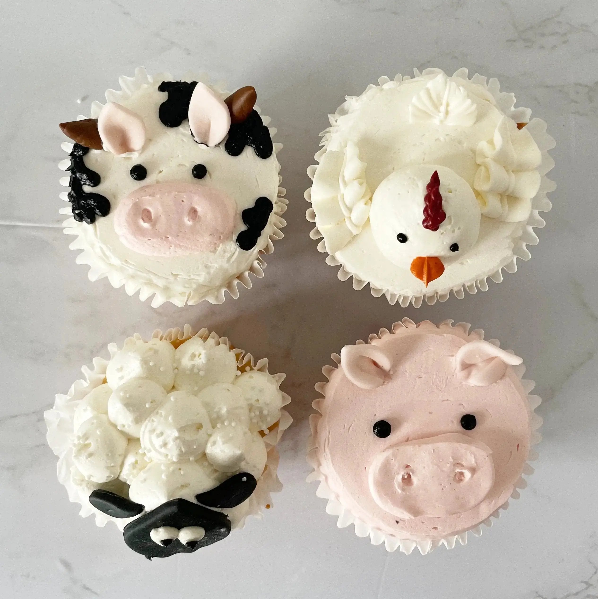 A close-up, top-down view of the four cupcakes decorated as farm animals.