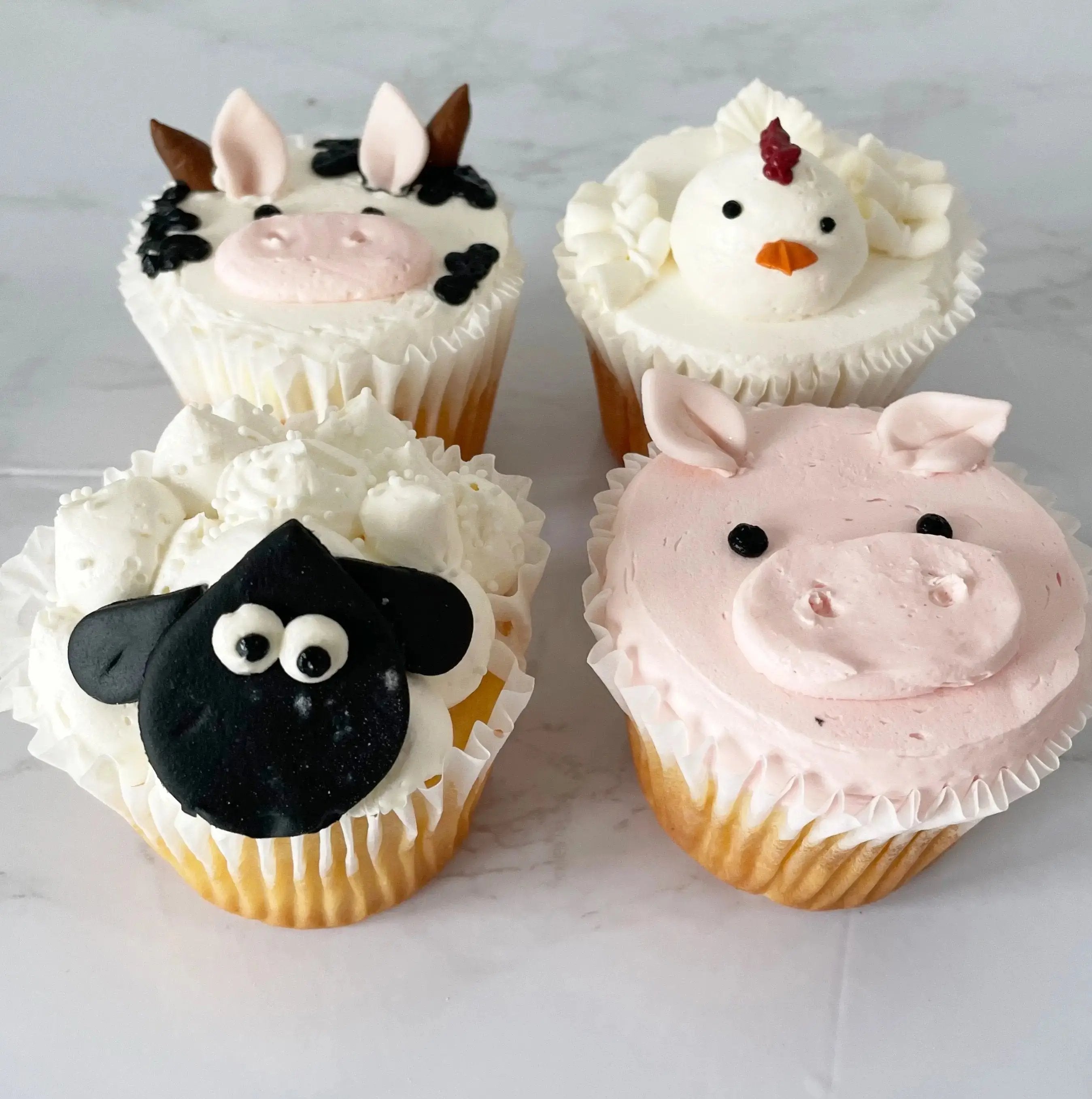 A close-up, top-down view of the four cupcakes decorated to look like farm animals.