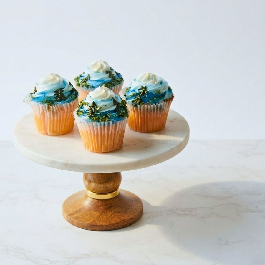 Cupcakes with blue and green frosting on a marble and wood stand against a white background