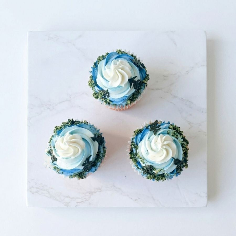 Three cupcakes with blue and white frosting on a marble surface