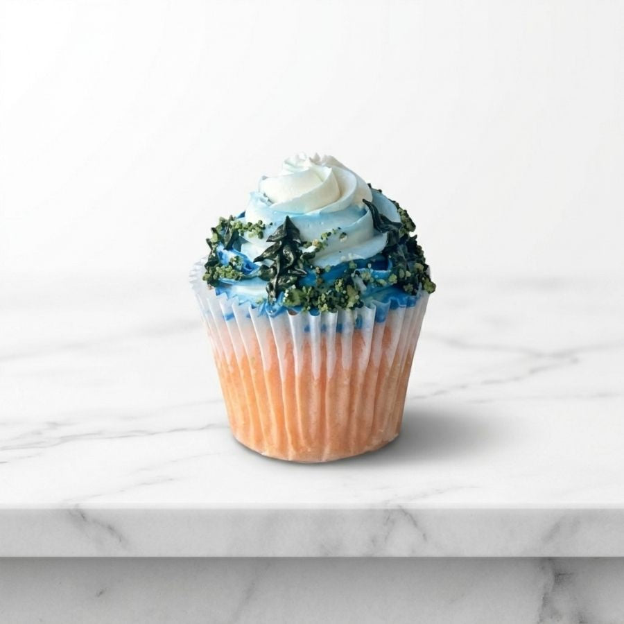 Cupcake with white frosting, blue decorations, and green leaves on a marble surface