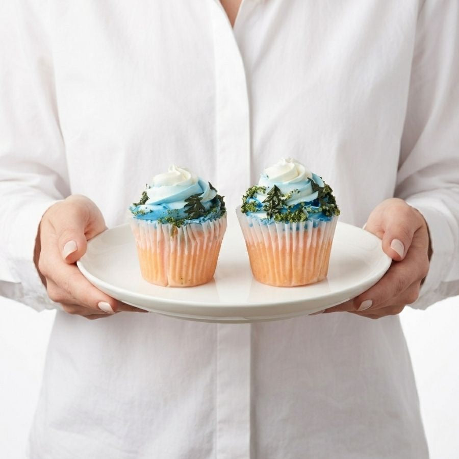 Person holding a plate with two cupcakes on a white background