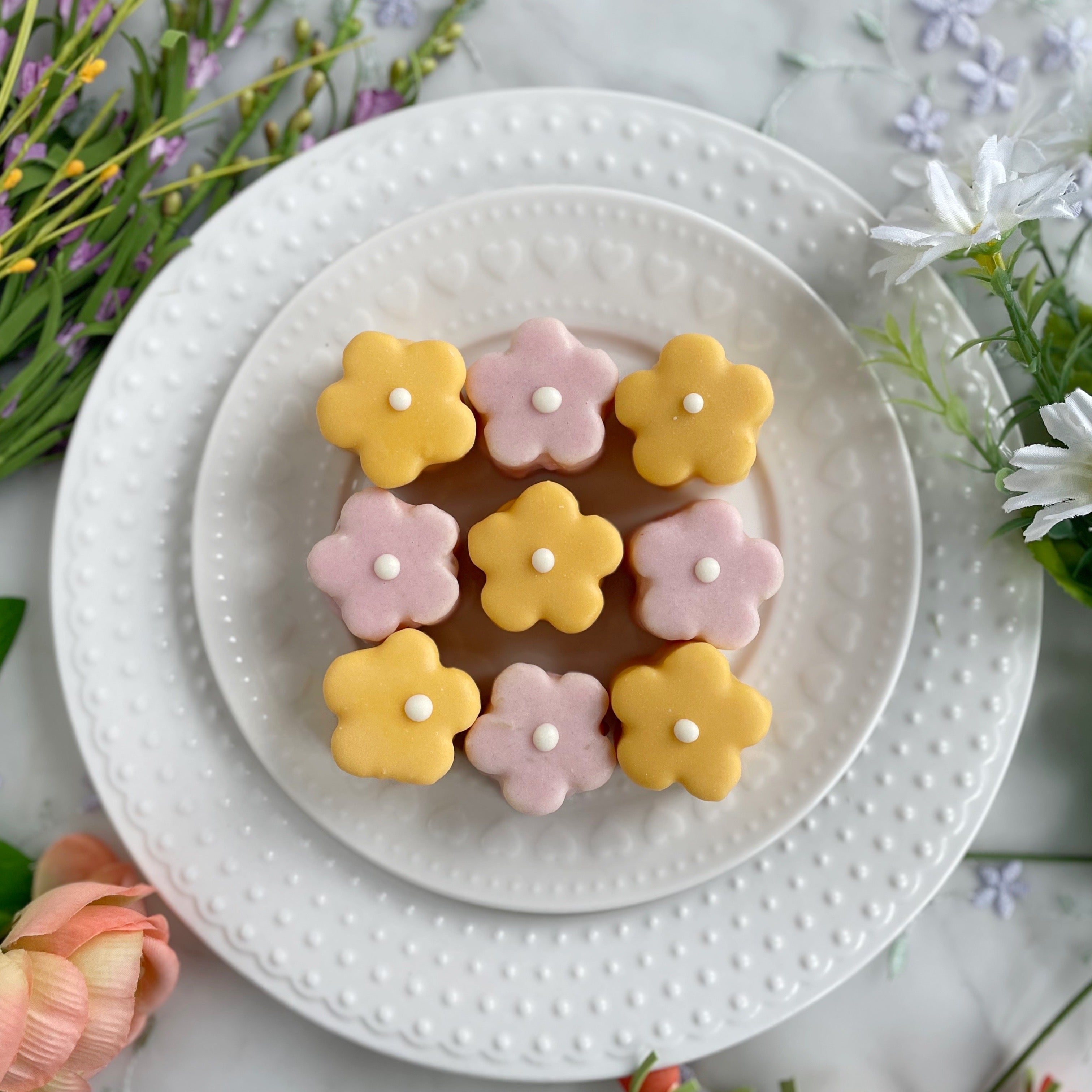 Overhead view of pastel-colored flower cookies arranged on a white plate outdoors
