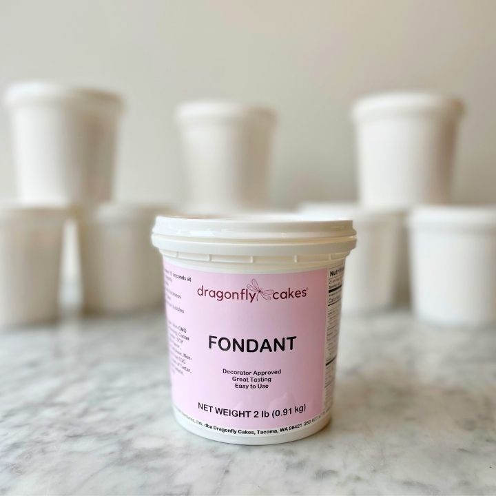 Container of dragonfly cakes fondant on a marble surface with blurred white containers in the background.