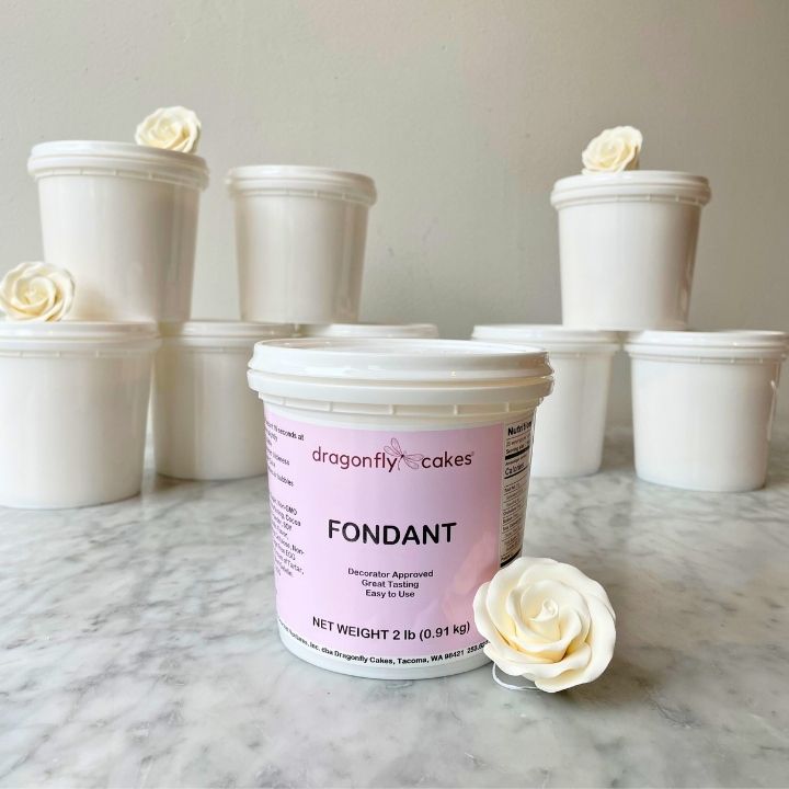 Container of dragonfly cakes fondant with white roses made from the fondant on a marble surface