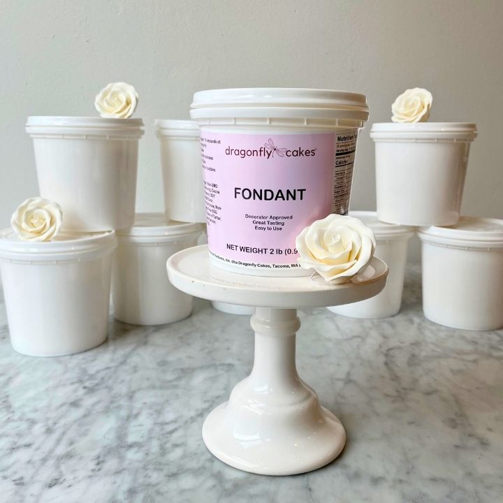 Container of dragonfly cakes fondant on a marble surface with white flowers.