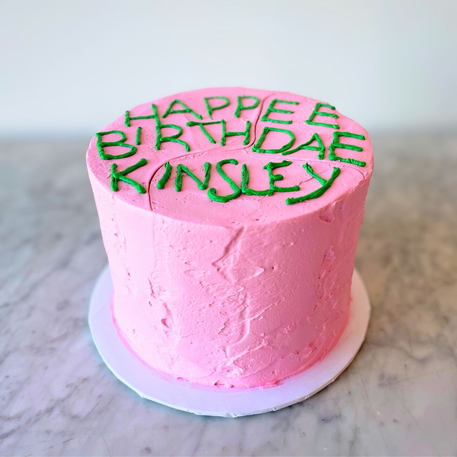 Pink birthday cake with green text inspired from the HP series on a marble surface