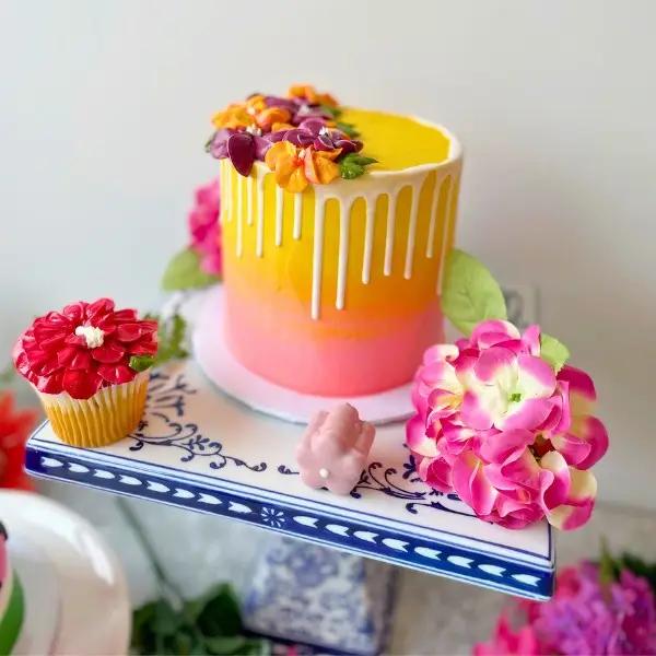 Colorful cake and cupcakes with floral decorations on a table.