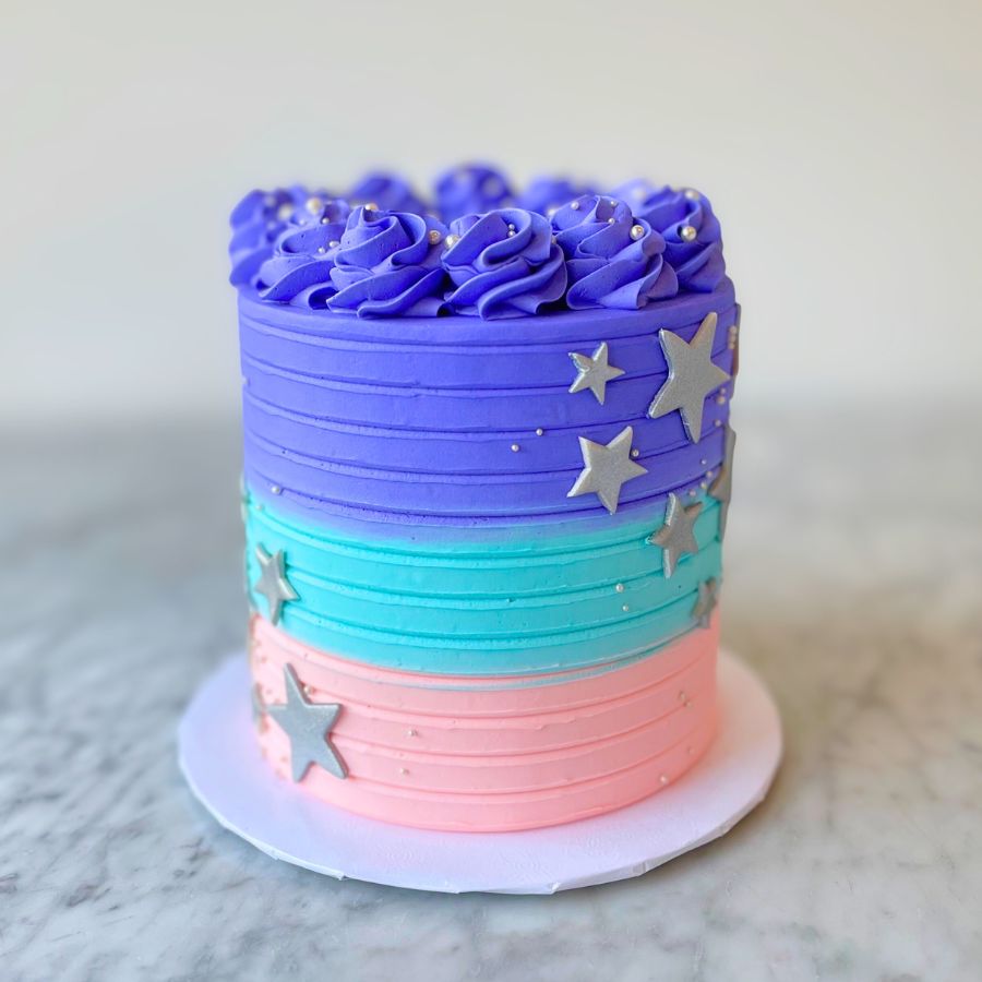 Colorful cake with purple, blue, and pink layers and star decorations on a marble surface.
