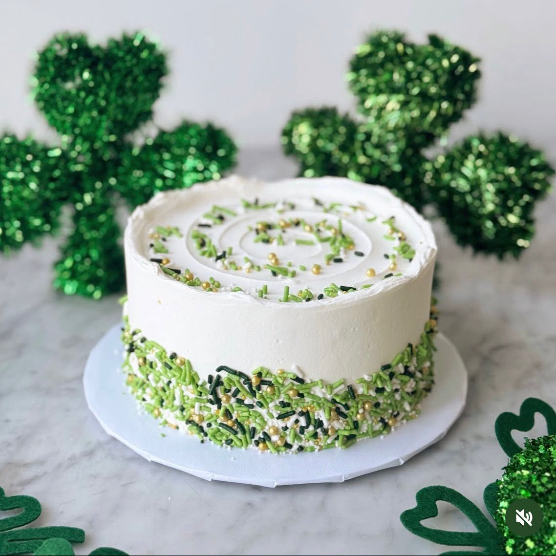White cake with green decorative elements on a marble surface with green shamrock decorations.