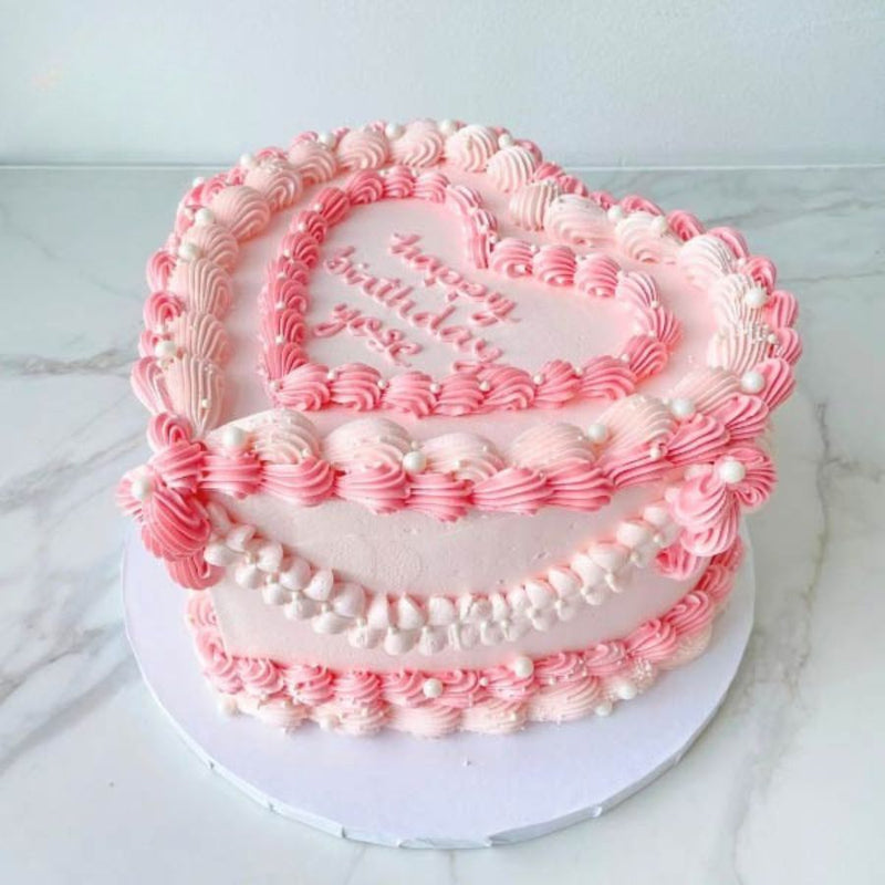 Two-tiered birthday cake with pink and white frosting on a marble surface
