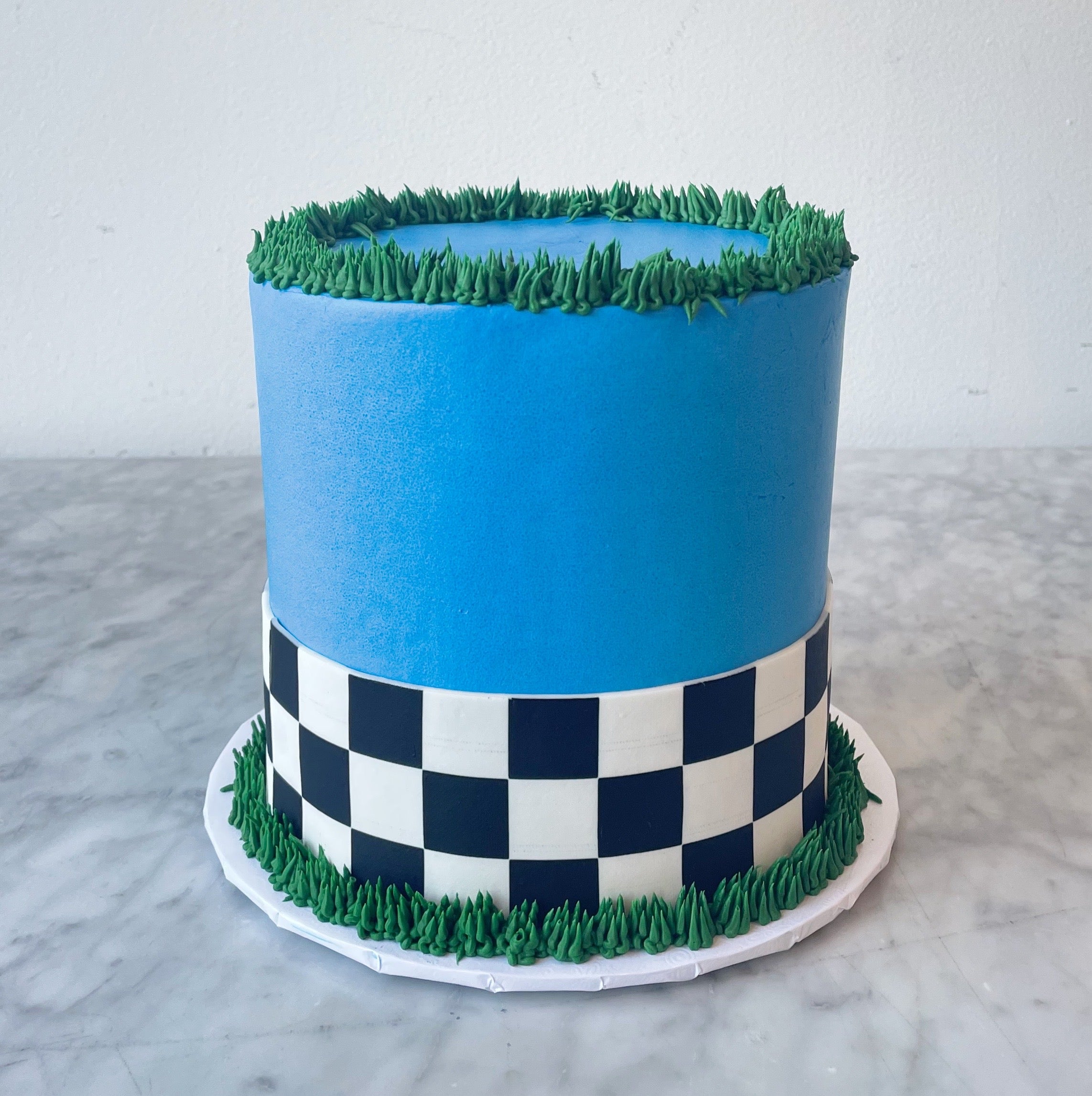 Blue cake with green grass-like top and checkered pattern on a marble surface