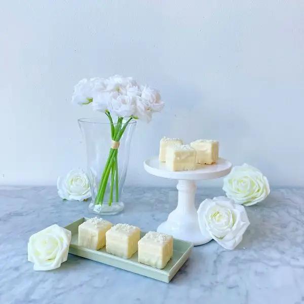 white square tea cake with white chocolate drizzle and edible pearls on a serving dish