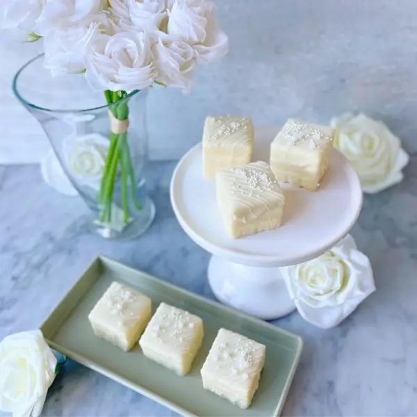 white square petit fours with white chocolate drizzle and edible pearls on a serving dish