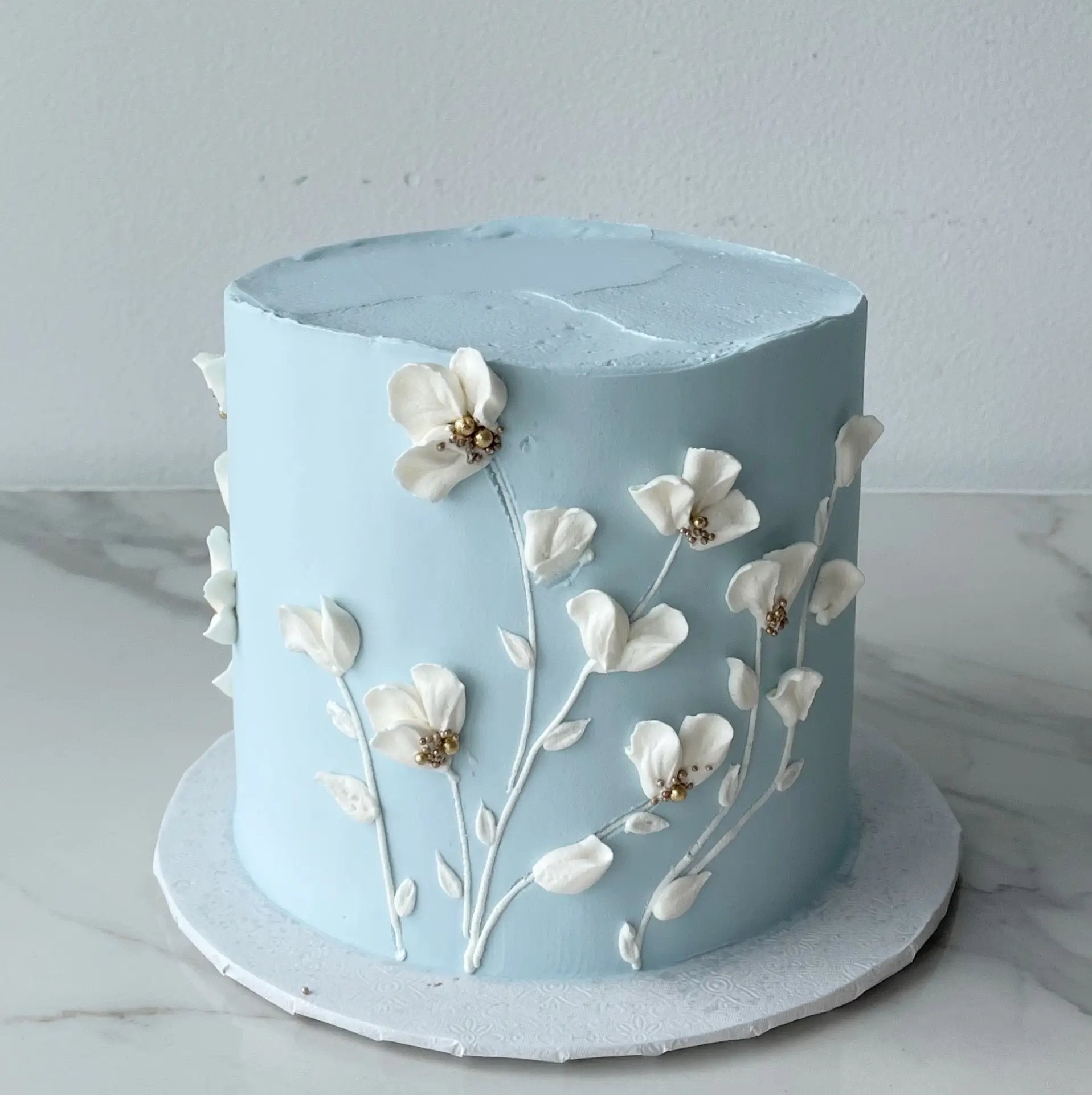 A decorated cutting cake with light blue buttercream and white petal designs on the sides, presented on a marble surface.