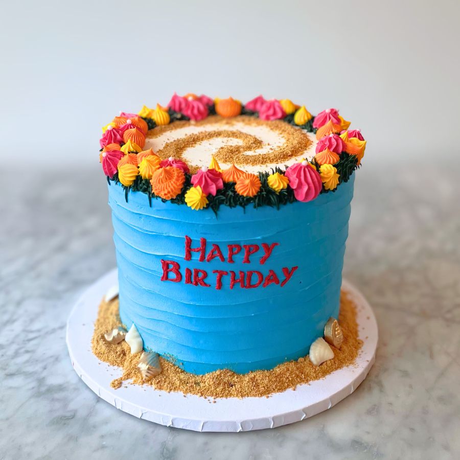 Blue celebration cake with colorful flowers and 'Happy Birthday' text on a marble surface